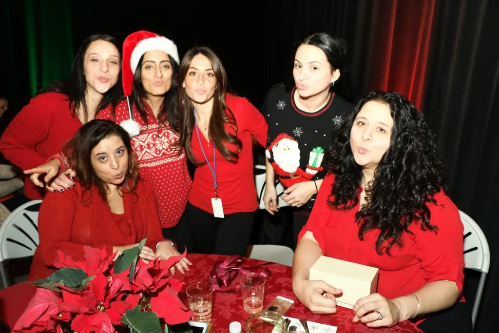 Coworkers in Santa hats and red outfits pose together at a corporate holiday party
