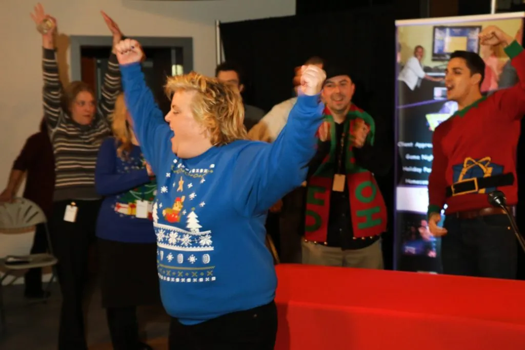 Employee in an ugly Christmas sweater cheers during a holiday party game show