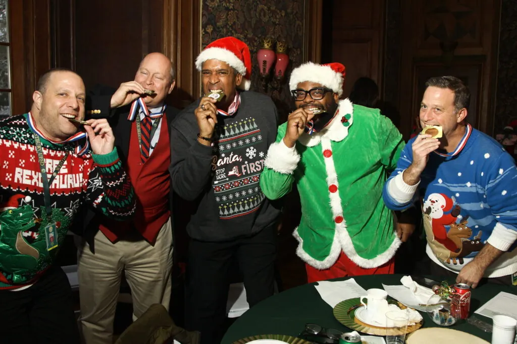 Coworkers in Santa hats and Christmas sweaters buzz in at a holiday trivia game show