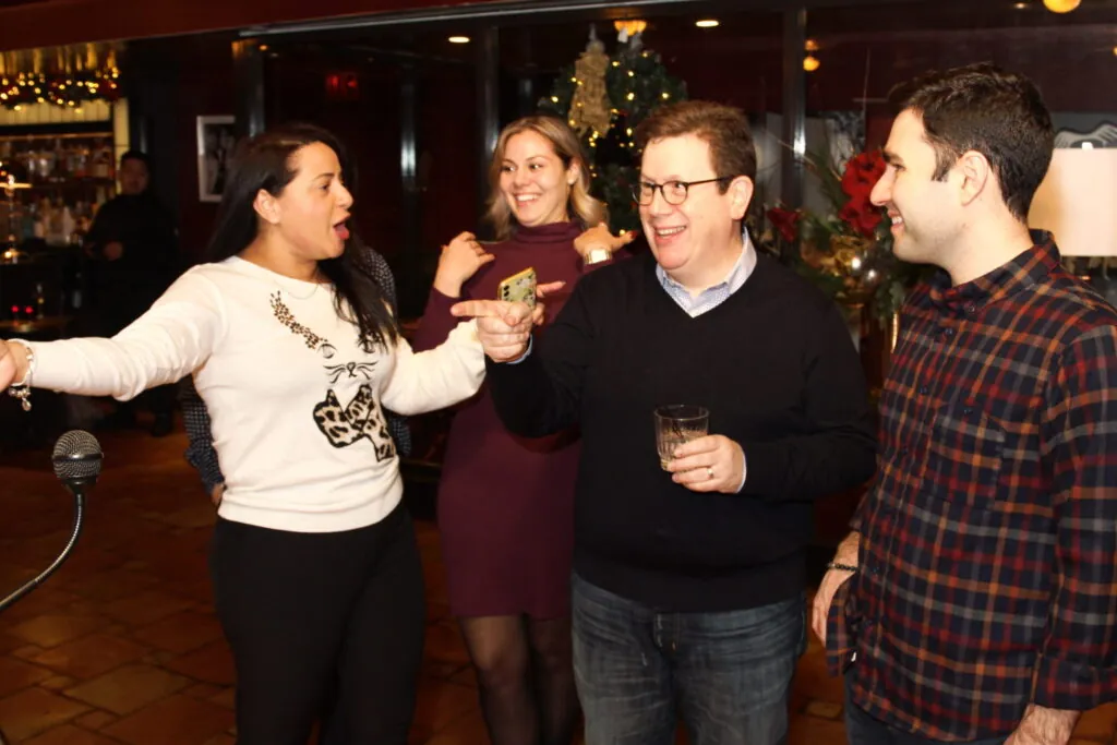 Coworkers in holiday sweaters celebrate during a game show team building activity