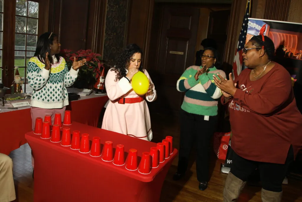 Employees play a cup-blowing holiday party game at work