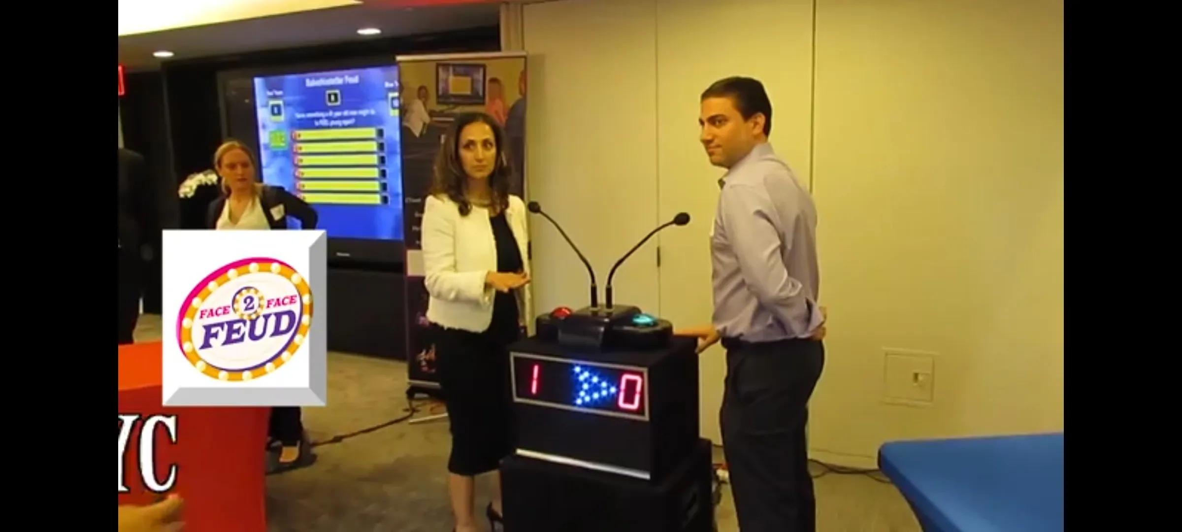 Face 2 Face Feud logo beside two players at the buzzer podium during a corporate game show, scoreboard reading 1 to 0